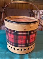 Side view of vintage round camping grill with red and black Scotch plaid tartan pattern, leather trim, and carrying handle