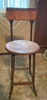 Front view of vintage industrial stool showing round wooden seat and metal curved backrest.