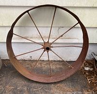 Front view of vintage metal wagon wheel showing 8 spokes and circular rim with rust.
