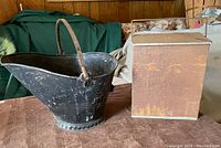 Photo of black metal coal or ash bucket with handle and vintage Taylor metal milk box side by side on table.