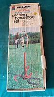 Original cardboard box with branding 'Billard Official Rodeo Model Pitching Horseshoe Set' showing an image of people playing horseshoes outdoors.