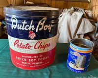 Front view of Dutch Boy Potato Chip can and Plus Coffee can on green table