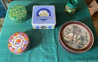 Photo showing five assorted vintage tins of varying shapes and designs arranged on a green surface.