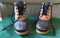 Front view of both boots showing brown upper, navy lace area, black rubber toe area with red accent line and navy laces.