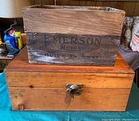 View showing the smaller Emerson Motor wooden box placed on top of the larger lockable wooden box, displaying the printed Emerson Motor branding on the smaller box and the latch on the larger box.