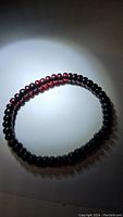 Single beaded amber bracelet under spotlight showing deep red translucent beads with some opaque beads.