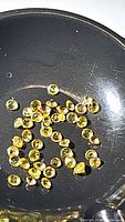 Close-up of multiple small calibrated round yellow Ceylon sapphires showing their diamond cut facets and bright color on a black surface.
