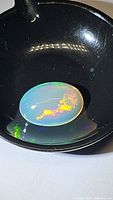Close-up photo of a polished oval cabochon Ethiopian opal with bright multicolored fire and flashes, sitting on a black surface.