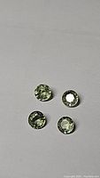 Four round cut moss green sapphires on a white surface seen from above, showing size and color variations.