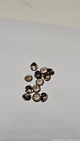 Top view of 14 small faceted smokey quartz gemstones on a white background showing their oval shape and brown smoky hue.