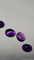 Four deep purple oval amethyst cabochons on a plain background showing color and shape.