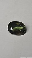Oval cut Australian forest green sapphire gemstone with green color and good clarity photographed on a neutral background.