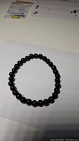 Black onyx beaded stretchy bracelet displayed on white paper background with lighting highlighting bead glossiness.