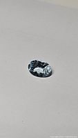Oval cut Brazilian aquamarine gemstone placed on a light surface capturing its clarity and color.