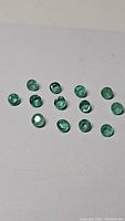 Top view photo of 14 natural round calibrated Zambian emerald gemstones arranged on white background showing their size and green color.