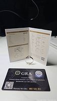 Photo of the moissanite ring displayed alongside GRA certificate and warranty card showing authenticity and warranty details.