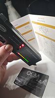 Moissanite gemstone certificate from GRA showing details and seller authenticity card with a diamond tester device actively testing the stone.