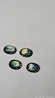 Four oval cut tri-colored sapphires showing varying blue, green and yellow hues under lighting on a neutral surface.
