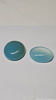 Two natural ice blue chalcedony gemstones with a smooth round and oval cabochon shape on a white background.