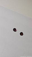 Two round cherry red garnet gemstones on white background showing facets and red reflections, confirming natural deep red color and quality.