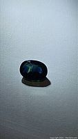 Photo showing oval natural blue green sapphire gemstone reflecting various shades of blue and green on a white background.