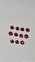Photo showing 11 small round cut natural rubies with deep red to pink hues and high luster on white background.
