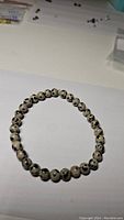 Photo of a stretchy bracelet consisting of Dalmatian jasper beads arranged in a circle on a white surface.