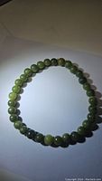 Photo of the natural green jade beaded stretchy bracelet laid flat showing the circular form and bead details under light.
