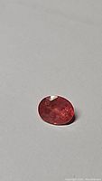 Front image of the oval cut pink-orange Padparadcha sapphire gemstone placed on a grey background, showing the gemstone's color and internal characteristics.