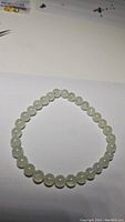 Photo showing natural prehnite round bead bracelet laid out in circle on white surface