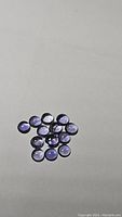 Cluster of 15 small round cabochon purple iolite gemstones shown on a plain background, well-lit to reveal color and shape.