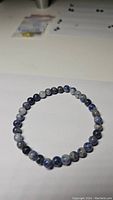 Natural blue sodalite stretch bracelet laying flat on a light surface, showing round polished gemstone beads with blue and white marbling.