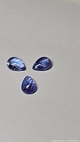 Three pear-shaped cabochon tanzanite gemstones showing natural purple-blue color and internal inclusions.