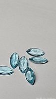 Six marquis cut Paraiba Blue Apatite gemstones shown on light background, displaying color and cut details.