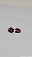 Pair of hot pink Umbalite Garnet gemstones in oval cut, approximately 6x5mm each, showing matching size and color.