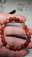 Close-up photo of natural red agate bracelet held between fingers showing bead size, color, and natural banding.