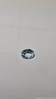 Single oval cut sky blue topaz gemstone on neutral background, showing clear light blue color and faceted cut.