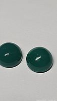 Two round vivid green onyx cabochon gemstones placed on a white surface under natural light showing their size and rich color.