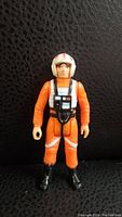 Front view of vintage 1977 Star Wars X-Wing Pilot action figure, showing detailed orange jumpsuit, life vest, and helmet with red stripe.