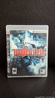 Front view of PlayStation 3 game case with Wolfenstein cover art featuring a cyborg soldier and logo.