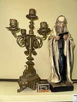 Photo showing brass candelabra and ceramic Rabbi figurine side by side with matchbox for scale.