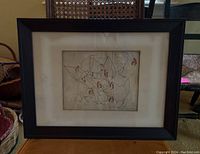 Framed print showing the full artwork with chickens, framed under glass with black wooden frame, placed on a table.