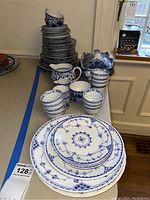 Photo showing stacked plates, cups, and tea pot with blue and white Asian style porcelain pattern.