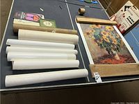 Photo showing multiple rolled posters and a large sunflower art print unframed lying on table