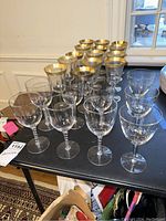 Image showing 16 stemware glasses of two types on a black table with some plates in the background.