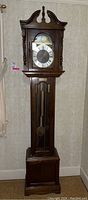 Front view of tall Emperor grandfather clock with dark wood finish, Roman numeral clock face, and moon phase dial.