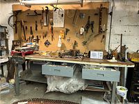 Wide view of workbench with pegboard holding various hand tools, clamps, radio, and hardware tools on surface and in drawers.