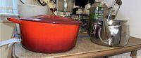 Red Le Creuset Dutch oven and stainless steel tea kettle sitting side by side showing exterior condition and colors.