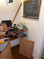 Overall view of chalkboard on wall above shelf with various desk supplies and cigar box with origami, plus cork bulletin boards leaning against the wall.