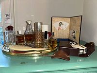 Full view of mirrored tray with perfume collection, electric shaver with case, leather hair tie, Asian folding screen, scissors, and lint brush